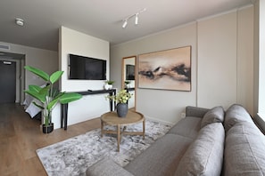 Un salon moderne avec un canapé gris, un téléviseur à écran plat fixé au mur, une table basse ornée d’un vase et un grand tableau abstrait.