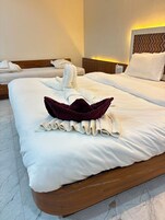 Habitación de hotel con dos camas, cada una con toallas ordenadas y un adorno encima.