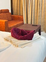 A bed with a white comforter and a folded red towel.