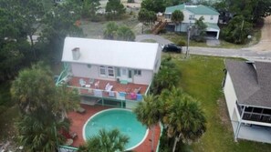 Ett hus med en swimmingpool, omgivet av palmer och en liten terrass med stolar.