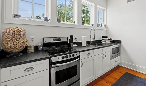 A modern kitchen with white cabinetry, a stainless steel stove, and a large window with a view of trees.