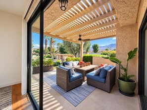 Eine Terrasse im Freien mit Korbmöbeln, einem Blumentopf und Blick auf eine angelegte Grünfläche.