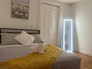 A bedroom with a bed, pillows, a blanket, a painting, and a door. - Cozy 3-bedroom Apartment- Family Friendly- Near Airport (Revere)