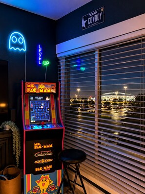 Ein leuchtendes Pac-Man-Spielgerät in einer Spielhalle, ein leuchtendes Geisterschild und ein Blick auf einen Parkplatz durch große Fenster.