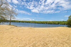 Una zona de playa arenosa con un lago y árboles al fondo.