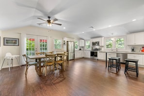 A spacious kitchen with white cabinets, a dining area with wooden chairs, and a ceiling fan. - Hilltop Hideaway · Sleeps 9 · Near Lake Hayward & Mohegan Sun (Colchester)