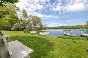 A lakeside property with a grassy area, picnic table, boats, and a house in the background.