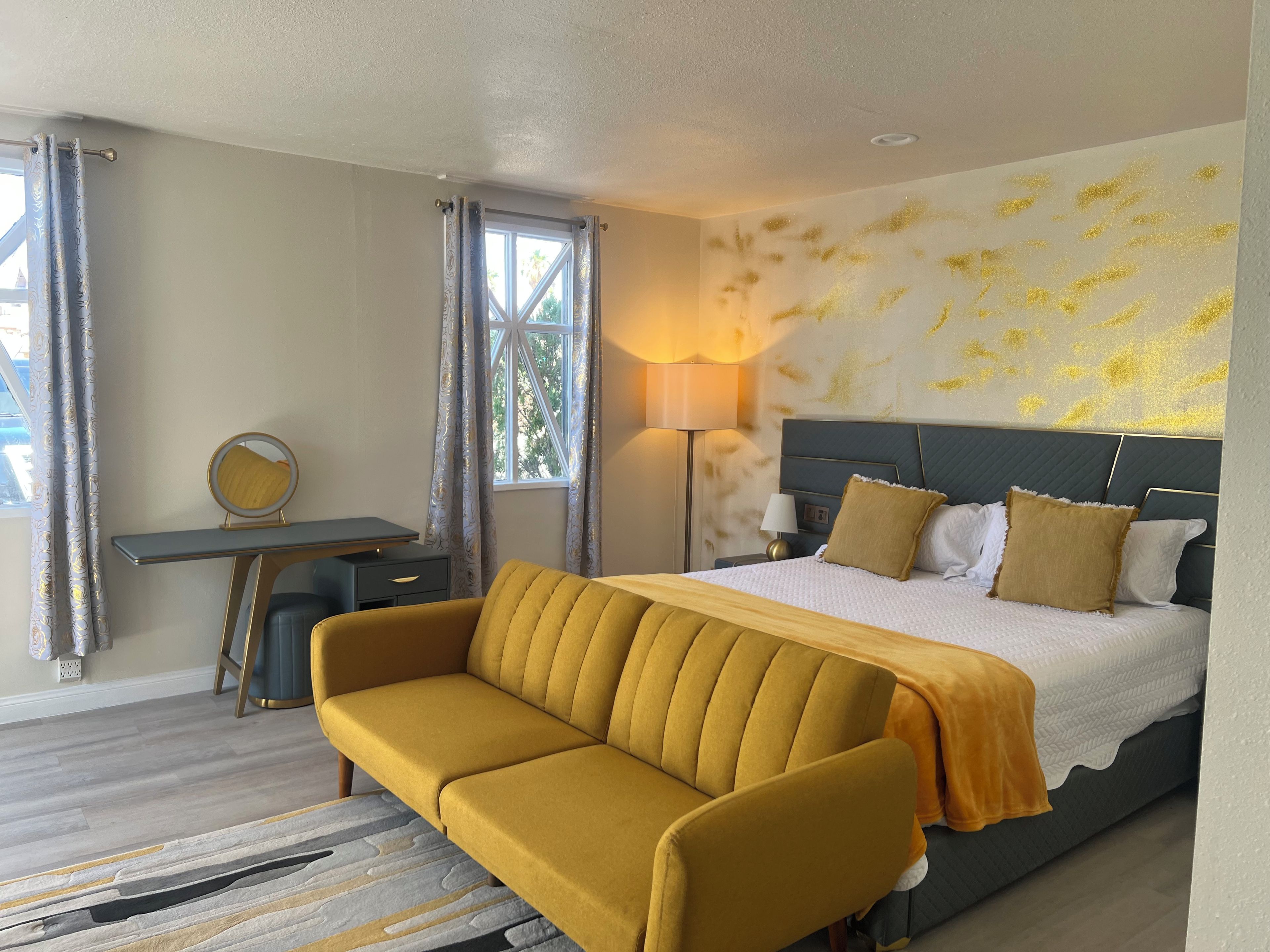 A hotel room with a bed, a sofa, a desk, a lamp, and a window with curtains.