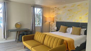 A hotel room with a bed, a sofa, a desk, a lamp, and a window with curtains.