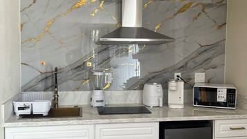 A modern kitchen with white cabinetry, a marble backsplash, and stainless steel appliances including a microwave, coffee maker, and blender.