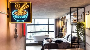 A modern bedroom with a large window, a neon sign, a bathtub, and a bed with a blanket and a teddy bear. - Romantic Studio at Mirante do Vale | Bathtub + 120" Cinema @cheng.du11 (São Paulo)