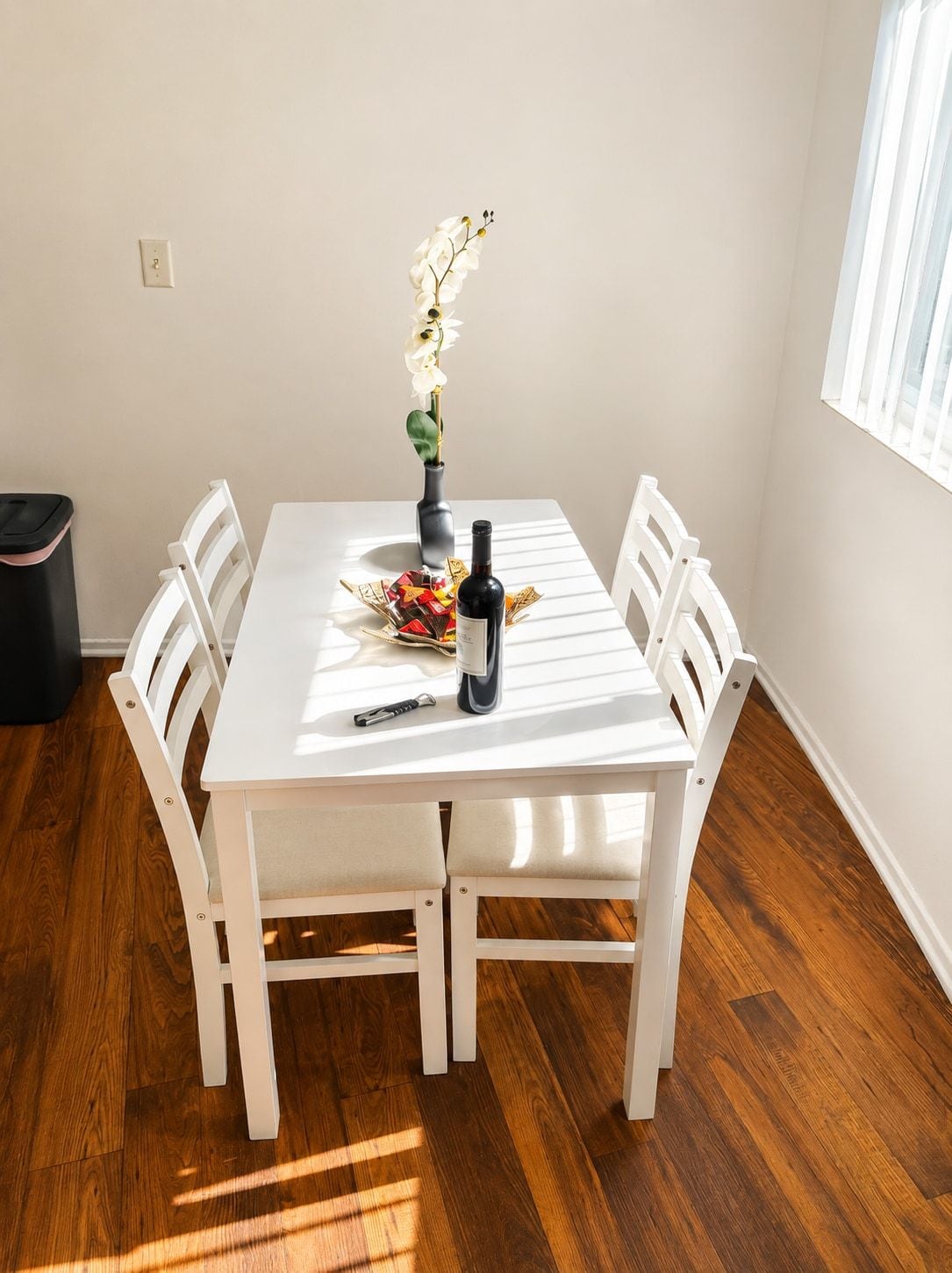 A dining table with chairs, a vase with flowers, a bottle, and a decorative item.