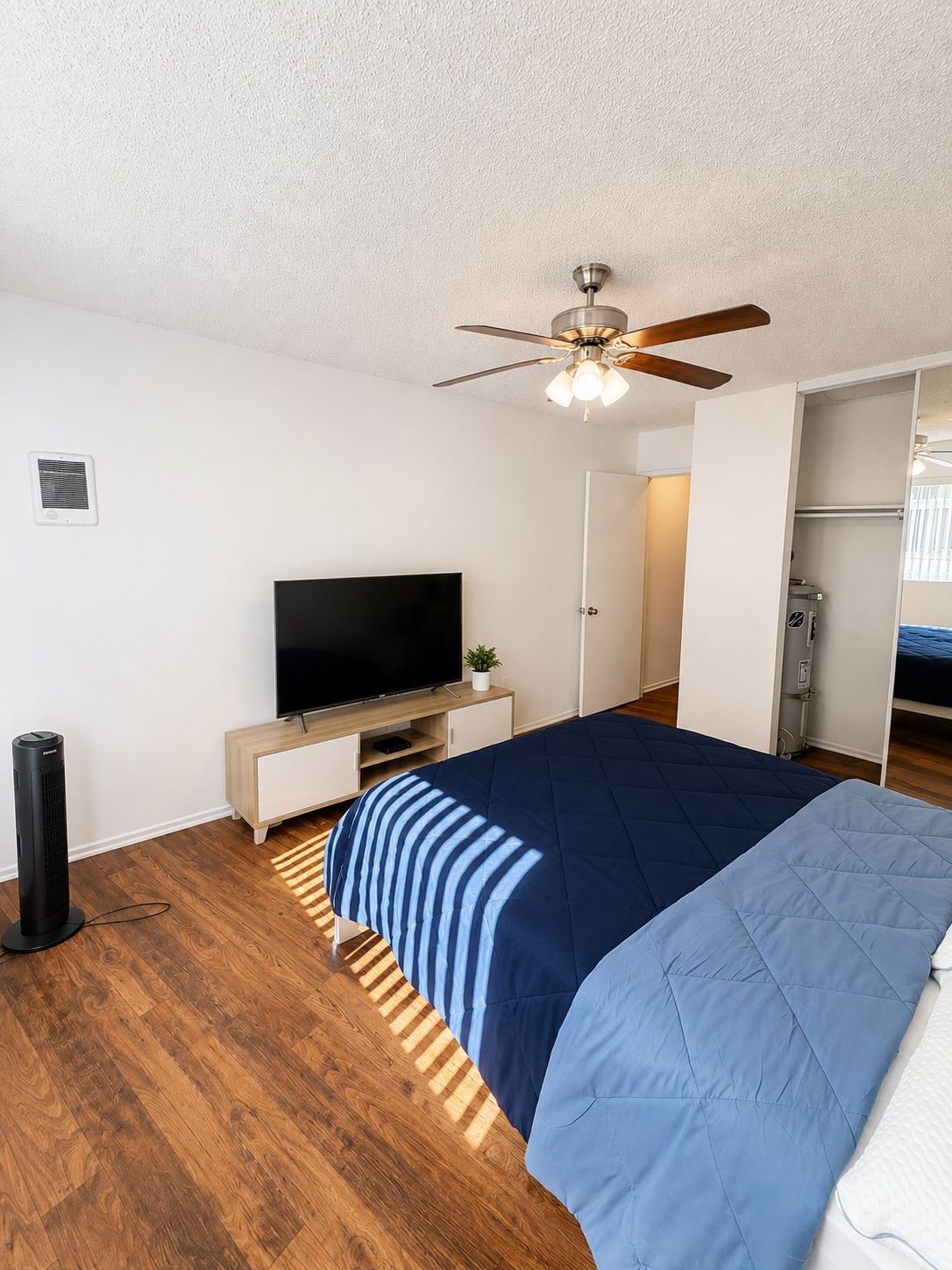 A bedroom with a bed, a television, a ceiling fan, and a wardrobe.