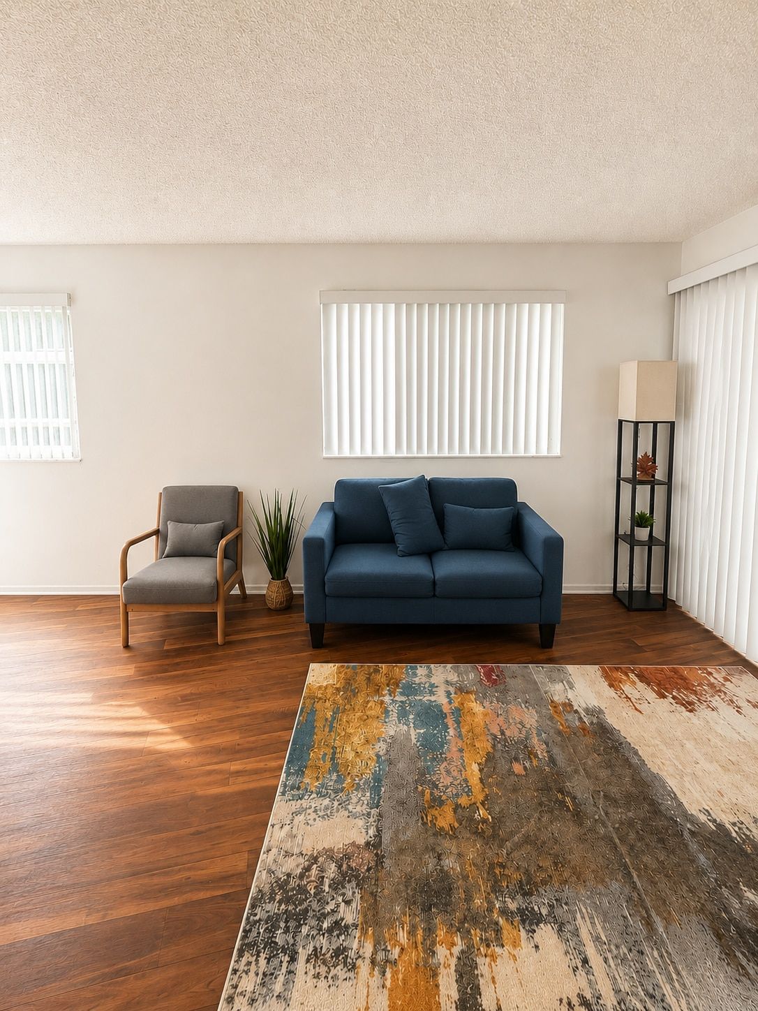 A living room with a blue sofa, a grey armchair, a wooden floor, and a large abstract rug.