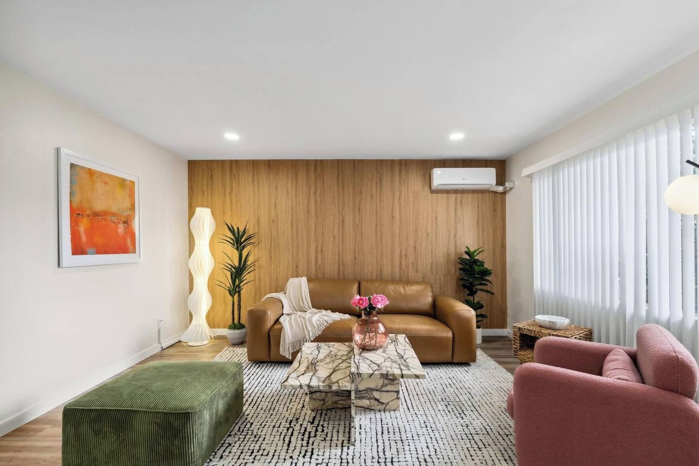 A modern living room with a brown sofa, a green ottoman, a pink armchair, and a coffee table with a vase of flowers.