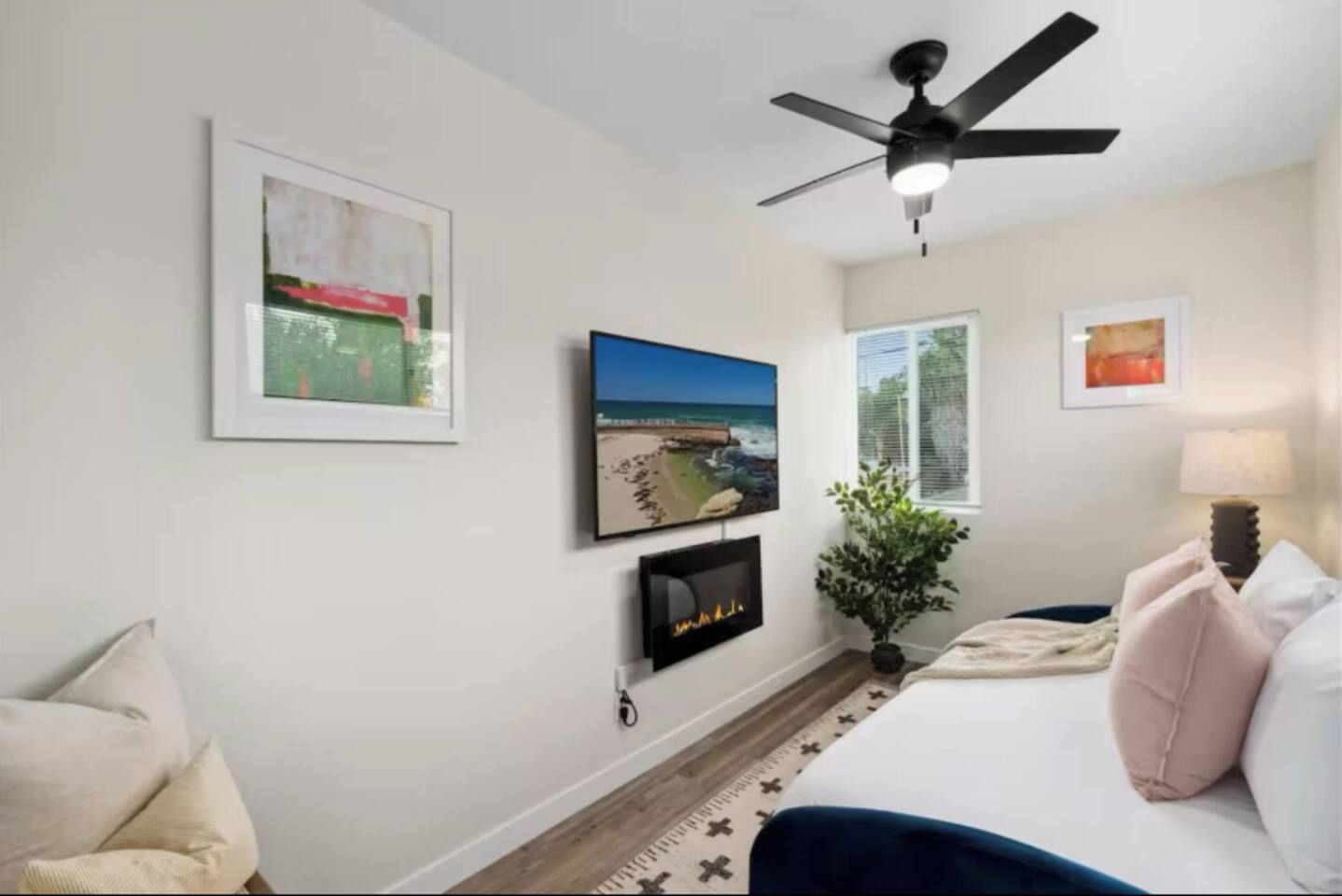 A bedroom with a bed, a ceiling fan, a fireplace, and framed pictures on the wall.