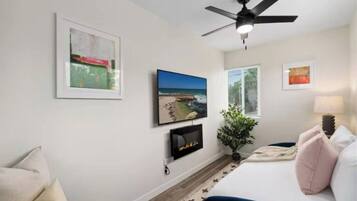 A bedroom with a bed, a ceiling fan, a fireplace, and framed pictures on the wall.
