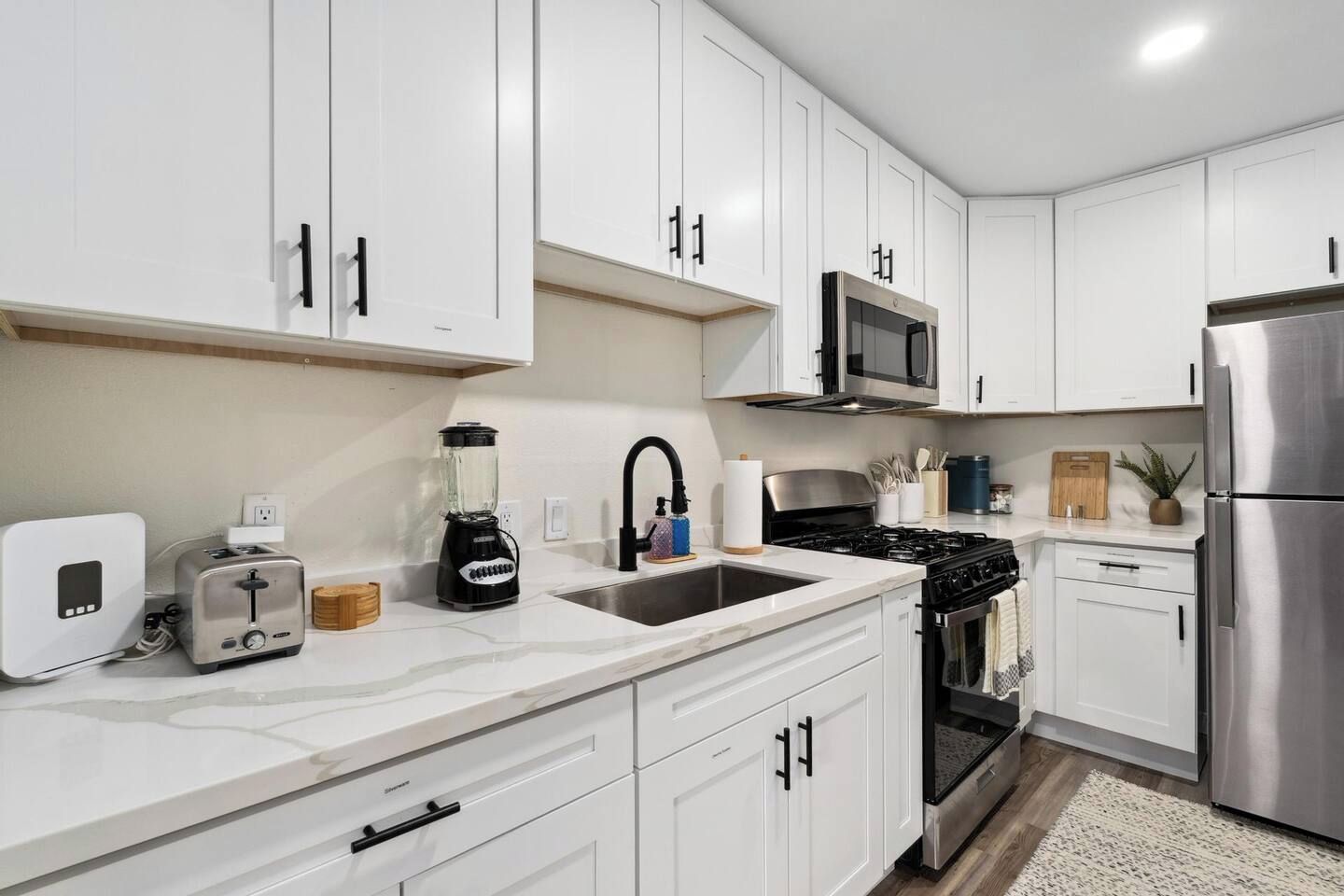 A modern kitchen with white cabinets, a stainless steel refrigerator, a built-in microwave, a gas stove, and a toaster.