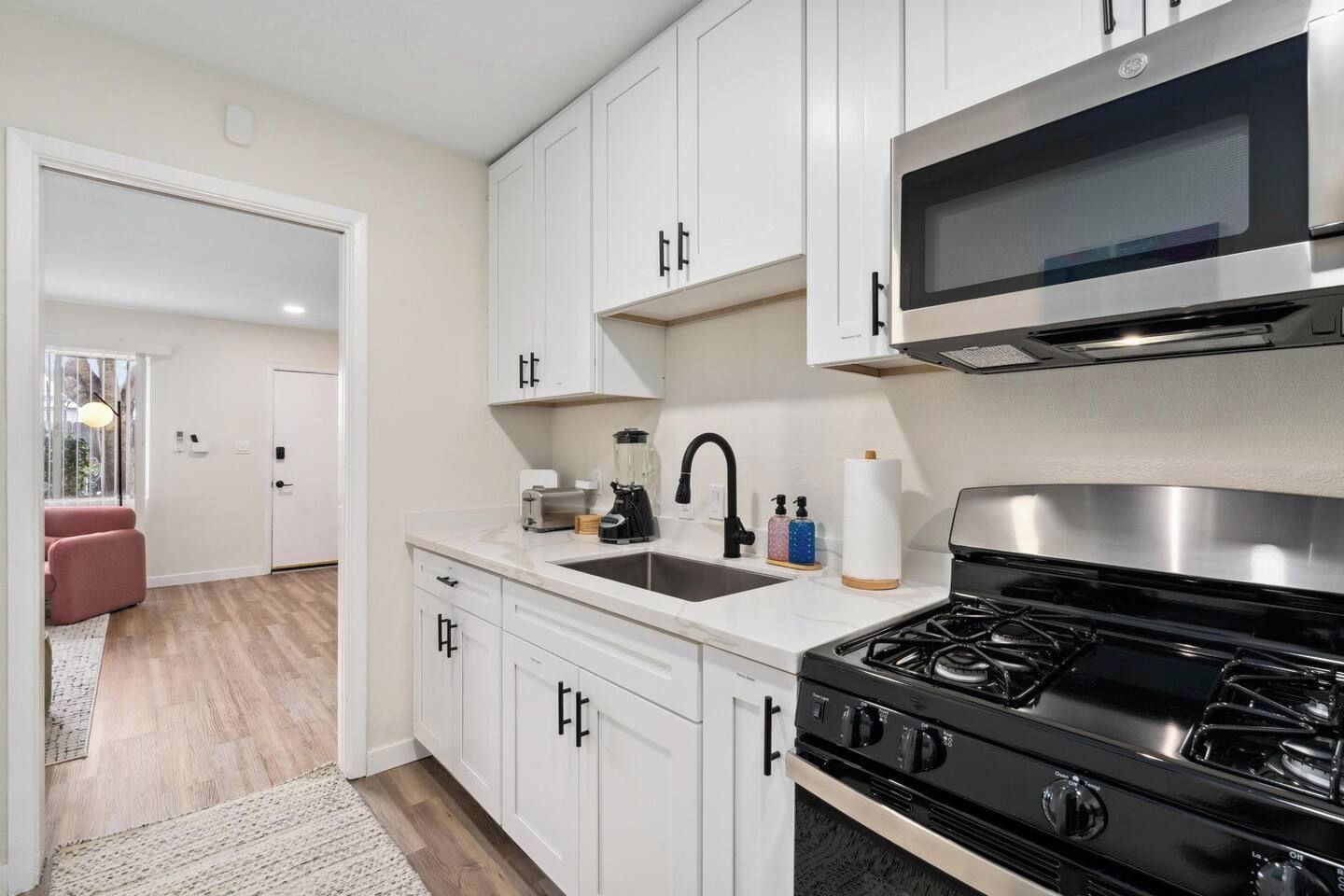 A kitchen with white cabinets, a black stove, a microwave, and a sink.