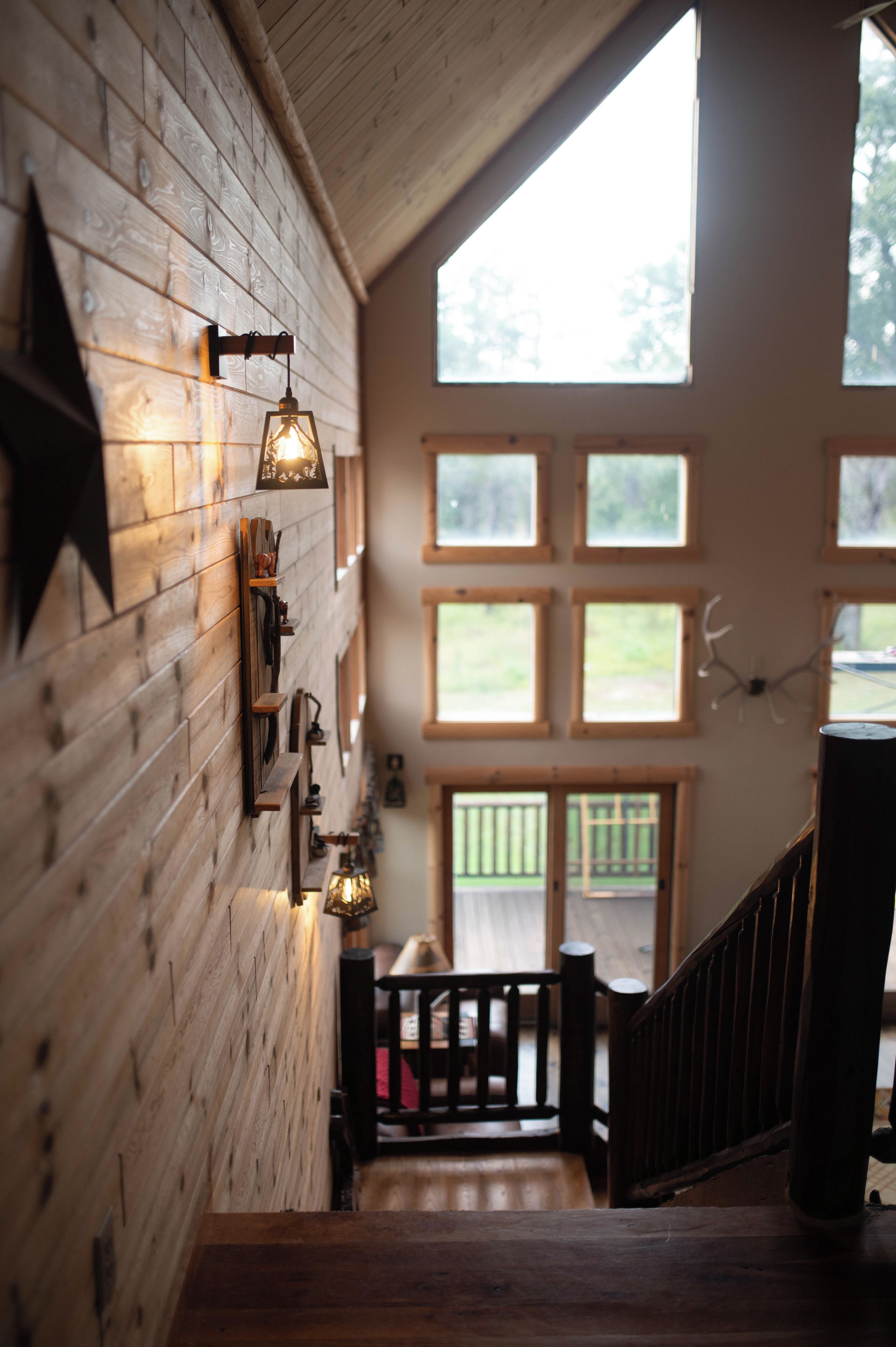 Un intérieur en bois avec un escalier menant à un balcon, agrémenté d’une décoration en forme d’étoile et de luminaires fixés au mur.