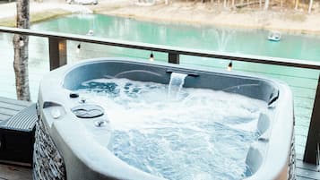 A hot tub on a wooden deck with a view of a lake and trees.