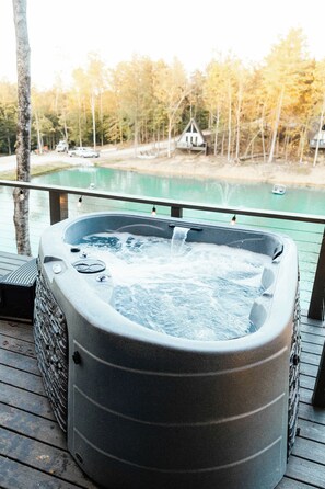 Ein Whirlpool auf einer Holzterrasse mit Blick auf einen See und Bäume.