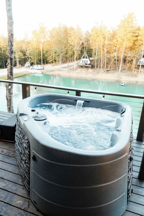 A hot tub on a wooden deck with a view of a lake and trees.