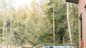 Une terrasse en bois avec un jacuzzi et un barbecue, entourée d’arbres.
