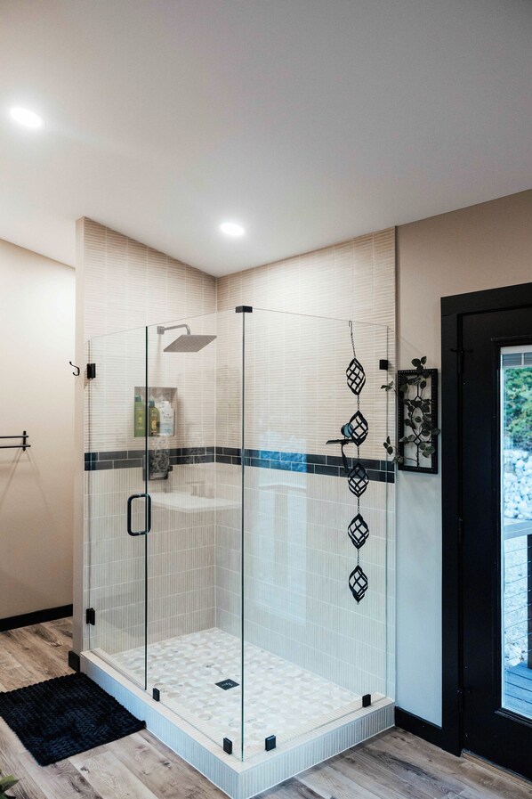Une douche moderne avec une porte en verre, une pomme de douche à pluie et un sol carrelé.