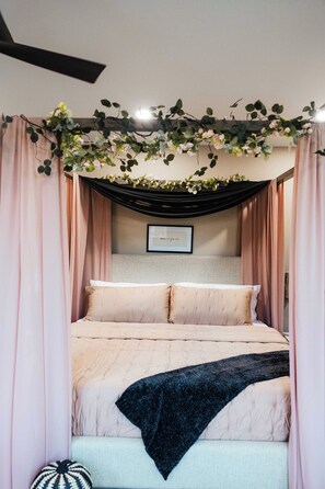 Un lit avec une tête de lit, des rideaux tombants et un tableau encadré accroché au mur.