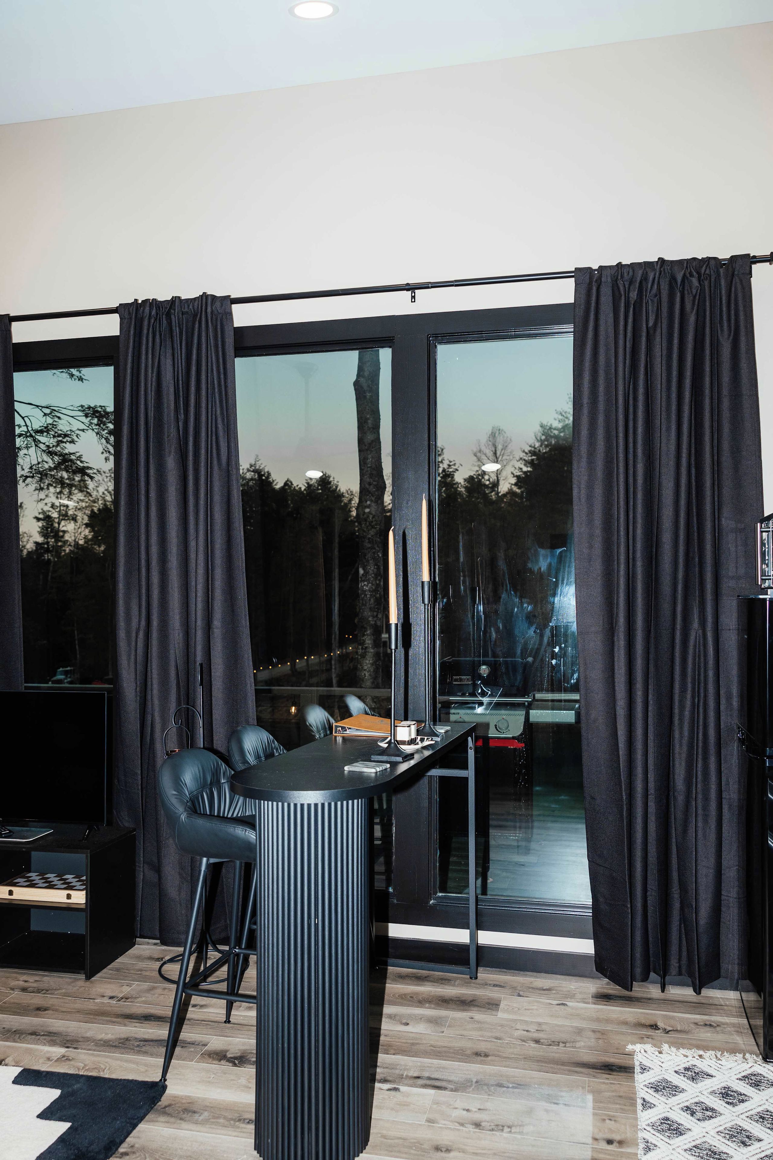 Un salon moderne avec un canapé noir, une petite table ronde et un téléviseur.