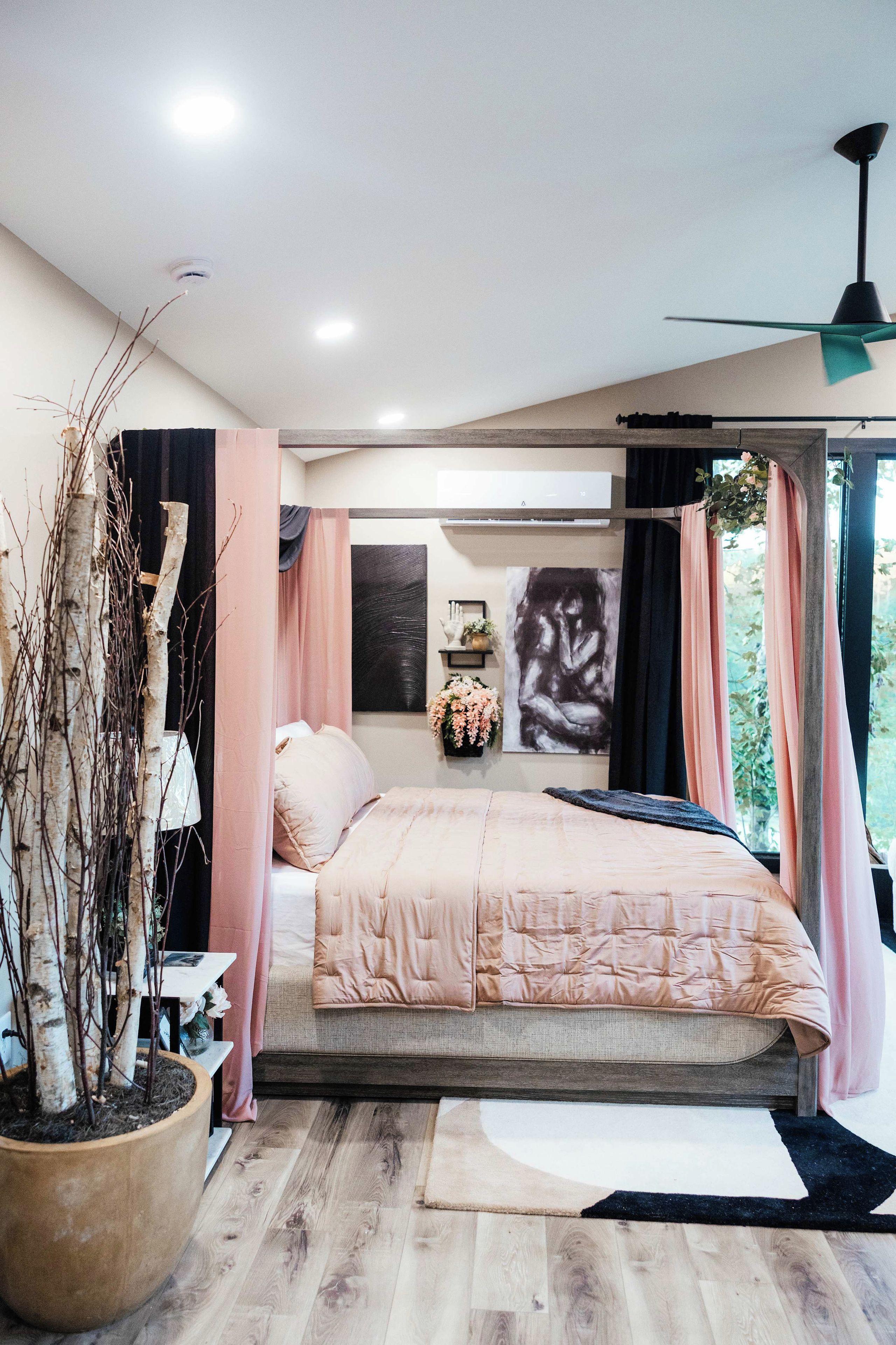 A bedroom with a bed, a potted plant, a ceiling fan, and a window with curtains.
