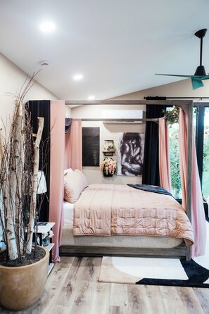 A bedroom with a bed, a potted plant, a ceiling fan, and a window with curtains.