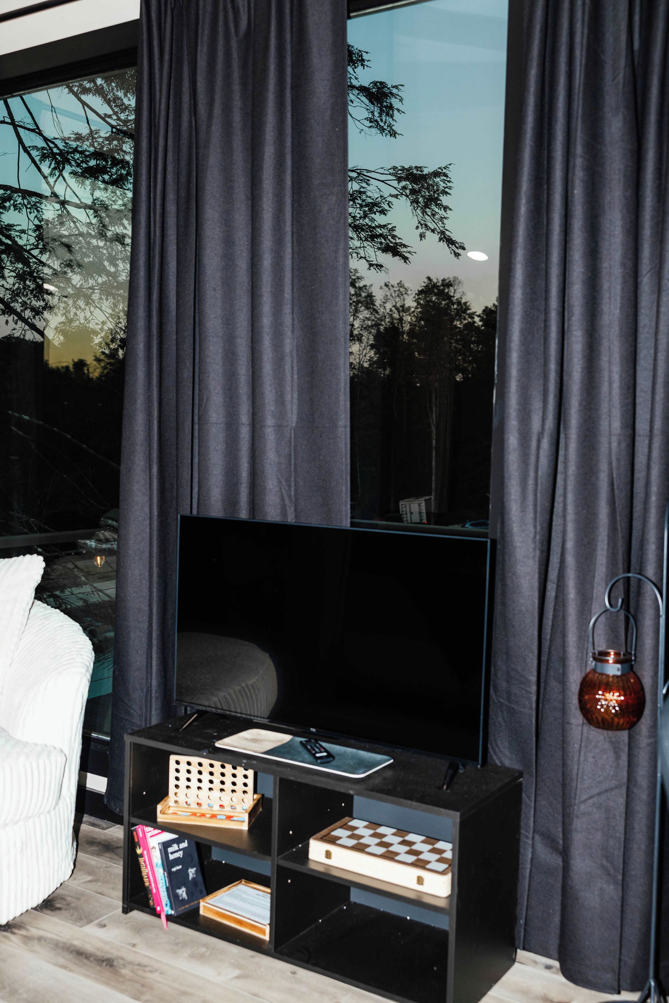 A modern living room with a flat-screen TV on a black stand, a chessboard, books, and a decorative lantern.