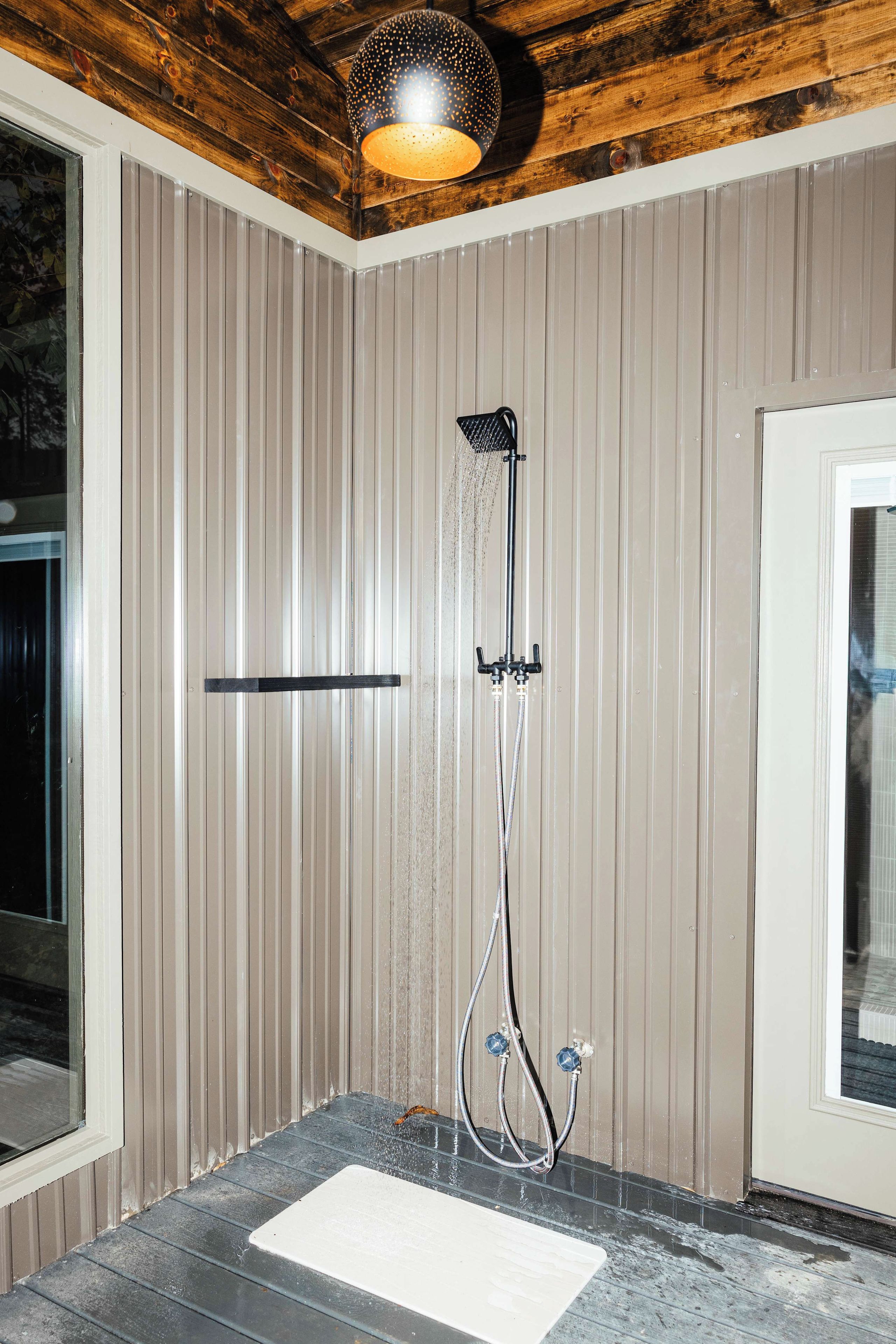 Un espace douche doté d’un mur avec un panneau vertical, d’un pommeau de douche à main et d’un pommeau de douche fixé au sol.