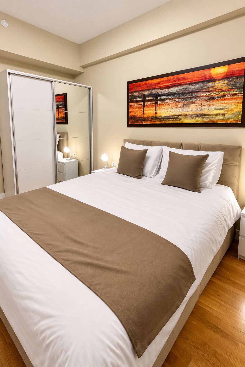 A neatly made bed with a brown throw blanket, a headboard, and a painting above it.