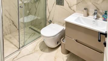 A modern bathroom with a glass-enclosed shower, a toilet, and a sink with a mirror above.