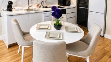 A modern kitchen with a dining area, featuring a round table with chairs, a refrigerator, and a microwave.