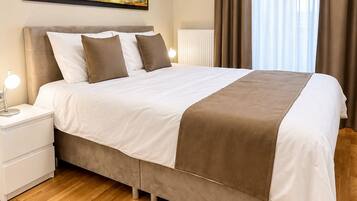 A hotel room with a large bed, a nightstand, a painting on the wall, and a window with curtains.
