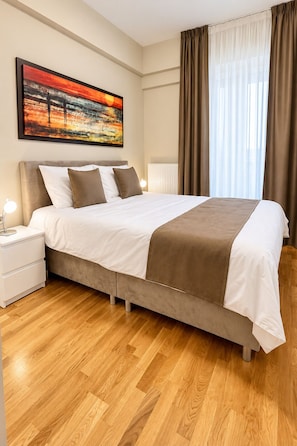 Una camera d'albergo con un letto grande, un comodino, un quadro appeso al muro e una finestra con tende.