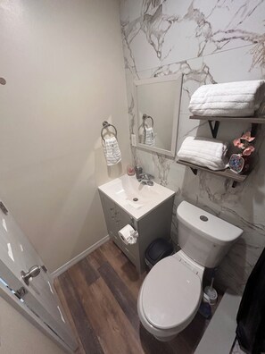A bathroom with a marble wall, a white sink, a toilet, and a shower area. - More than just a place to rest. (Tampa)