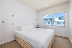 Ein Hotelzimmer mit einem großen Bett, einem Fenster mit Blick auf Gebäude und einem kleinen Nachttisch mit einer Lampe.