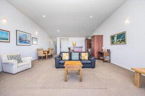 A spacious living room with a black leather sofa, a white armchair, a wooden coffee table, and a dining area with a table and chairs. - Dual-Level Harbour Apartment on The Wharf (Auckland City)