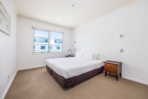 A bedroom with a large bed, a nightstand, a window, and a view of buildings outside. - Dual-Level Harbour Apartment on The Wharf (Auckland City)