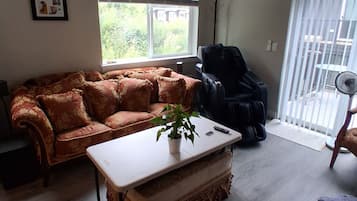 Ein Wohnzimmer mit einer Couch, einem Massagesessel, einem Couchtisch und Blick ins Freie durch ein Fenster.