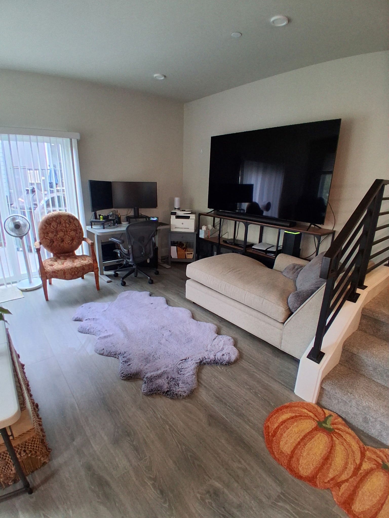 A living room with a sofa, a television, a desk with a computer, and a staircase.