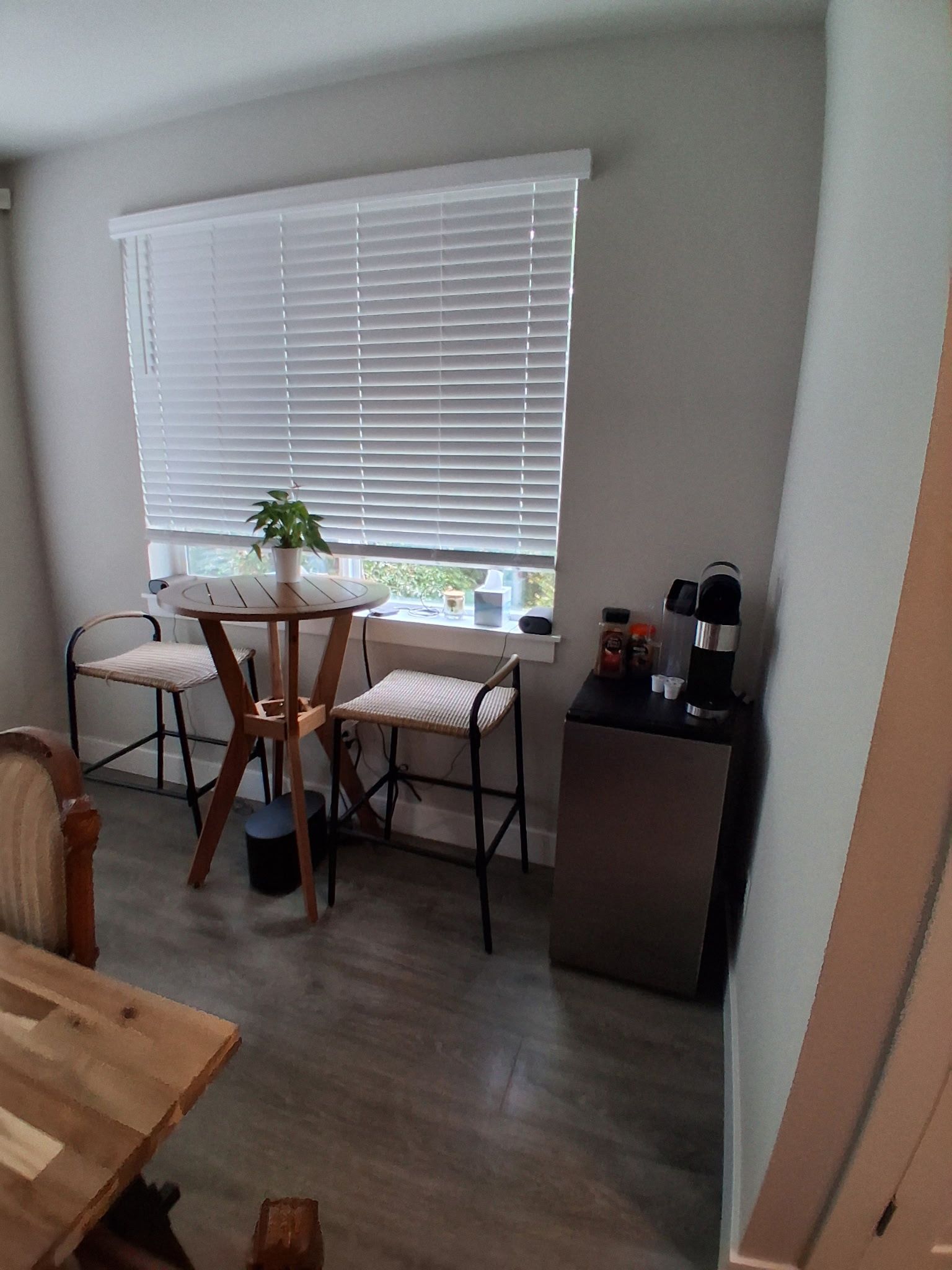 A compact kitchen with a dining table, chairs, a small refrigerator, and a window with blinds.