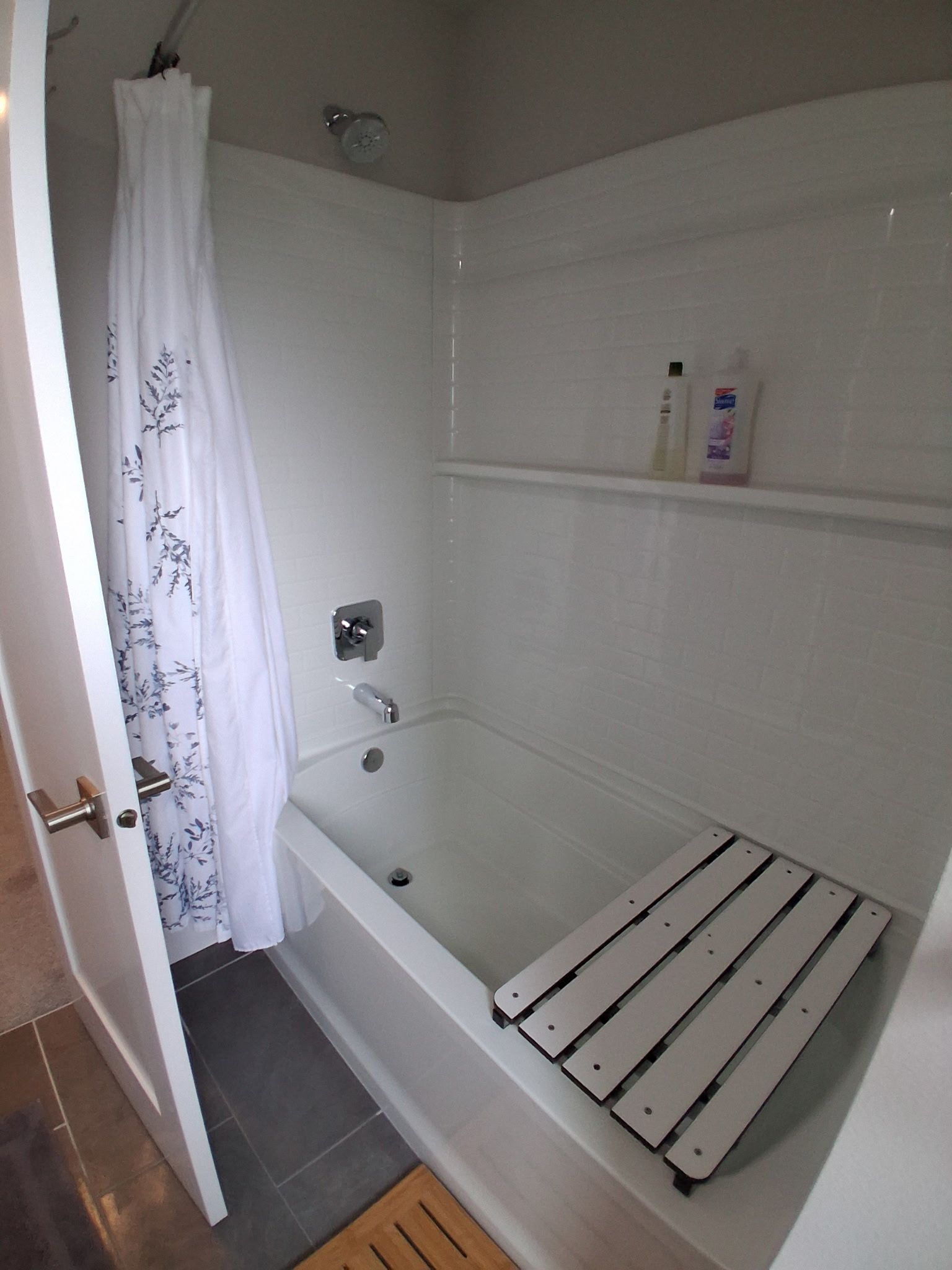 A bathroom with a bathtub, a shower curtain, and a shelf with toiletries.