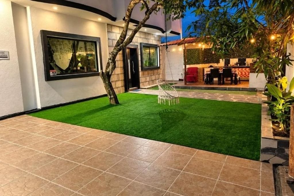 A patio with artificial grass, a hanging chair, and a dining area with tables and chairs.