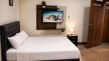 A hotel room with a bed, a television mounted on the wall, a bedside table with a lamp, and a wooden door labeled 'SEA LION'.